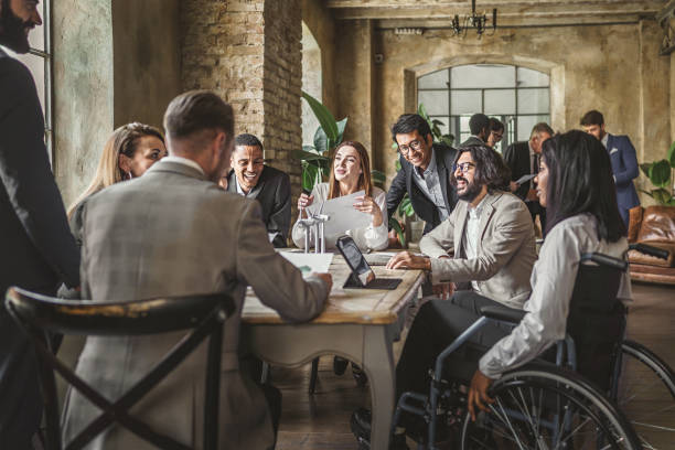 Multiracial group professional business workers in suit with people with disabilities on the wheel chair discussing sitting around the meeting table of the office about sustainable and renewable green energy - business lifestyle